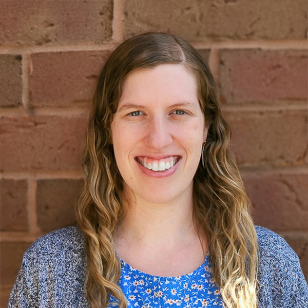 Skye Hookham, Resident Services Director at University Senior Living, smiling in front of a brick wall while wearing a blue floral top and a textured cardigan.