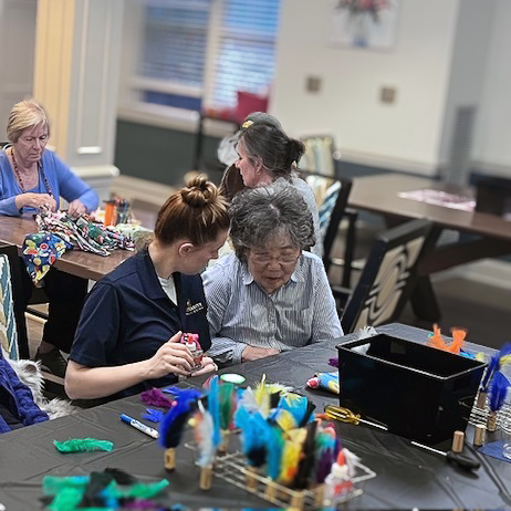 Senior residents enjoy an arts and crafts session with colorful feathers and supplies, supported by team members.