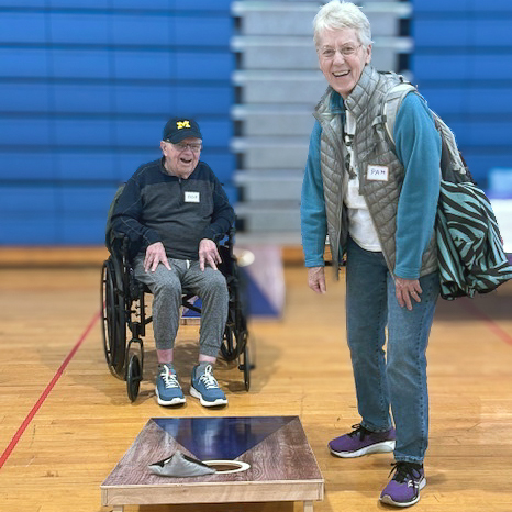 Senior residents smile while playing a game of cornhole in the gym, enjoying friendly competition and staying active.