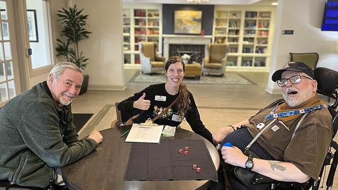 Resident Services Director at University Senior Living enjoys a tabletop game with two smiling senior men.