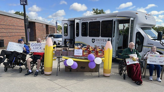 Residents from University Senior Living hold up encouraging signs amid decorations and a heartfelt display for returning students at a local school.
