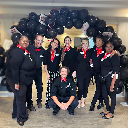 Team members dressed in black and red smile under a balloon arch.