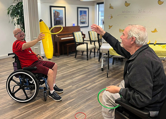 Two residents at University Senior Living play a Wellness game of tossing rings onto an inflatable banana.