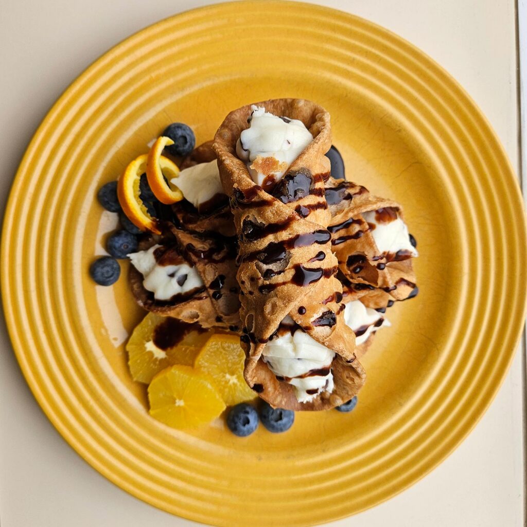 Delicious, chocolate-drizzled cannoli and fresh fruit atop a harvest yellow plate.