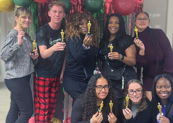 A group photo of University Senior Living team members smiling during a festive celebration, holding small gold trophies.