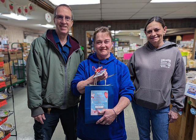 Local business owners smile in their establishment, one woman holding a gift bag given by University Senior Living.