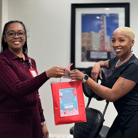 A woman on the University Senior Living team presents a gift bag to a local business owner for Small Business Day, both smiling brightly.