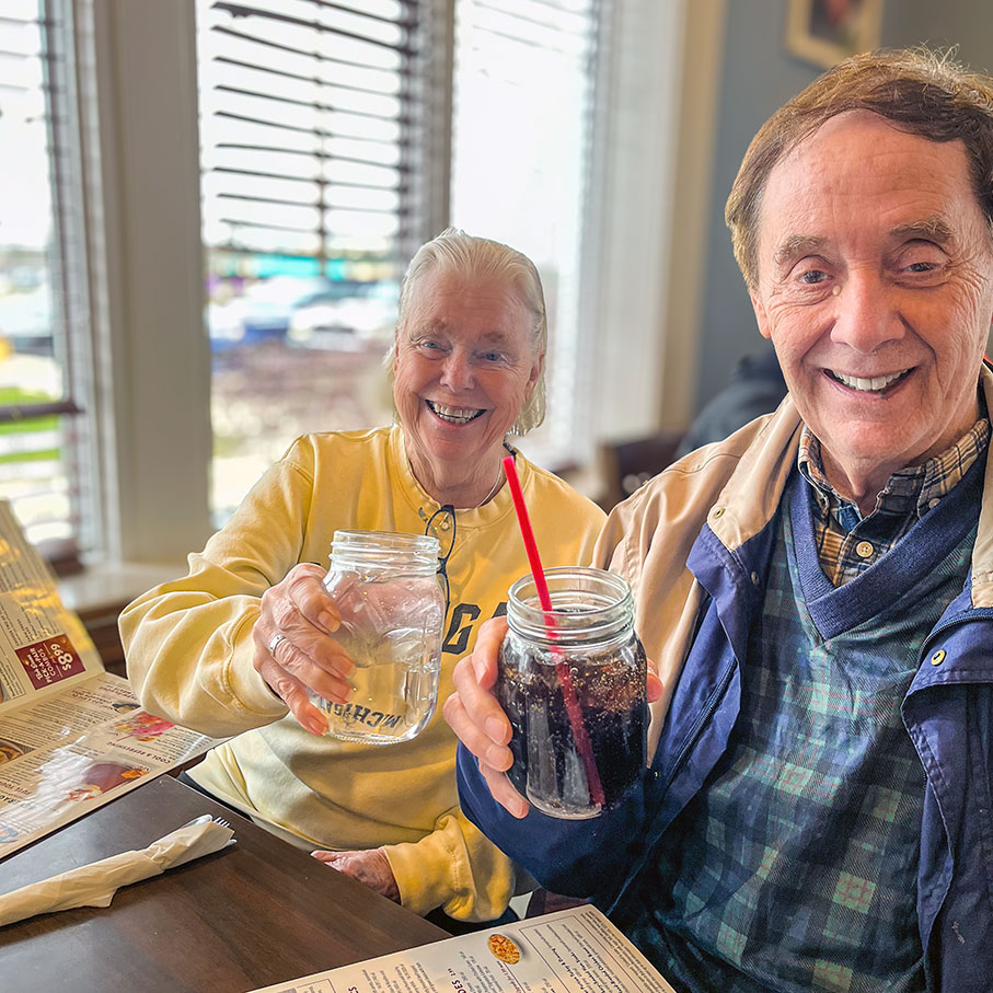 A senior man and woman from University Senior Living enjoy a meal at a local establishment, smiling brightly.