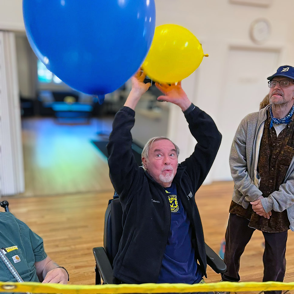 A resident at University Senior Living reaches up animatedly, playing balloon volleyball.